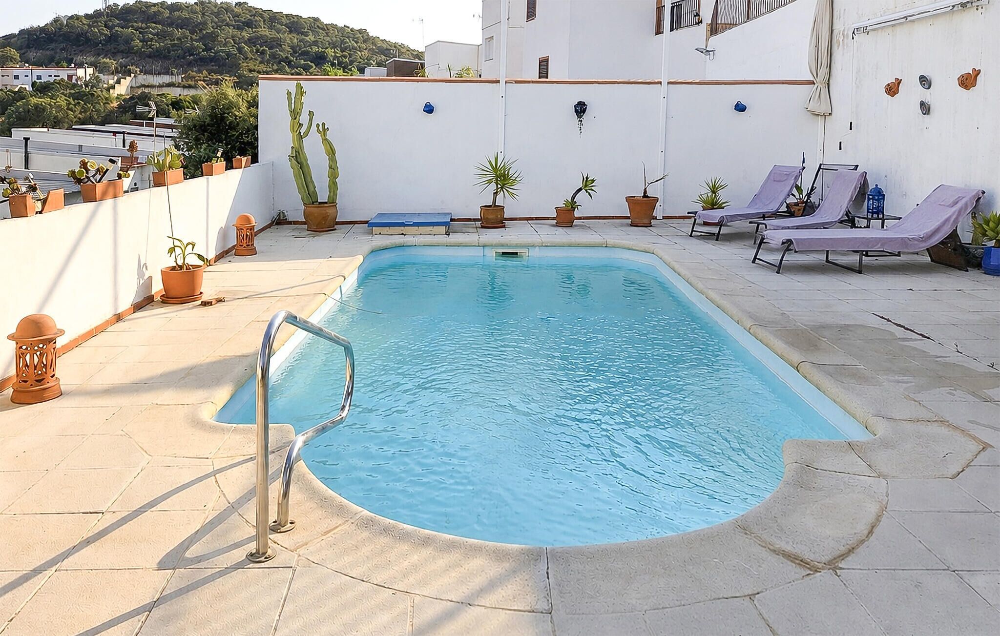 A rooftop swimming pool with a metal ladder, potted plants, and lounge chairs.