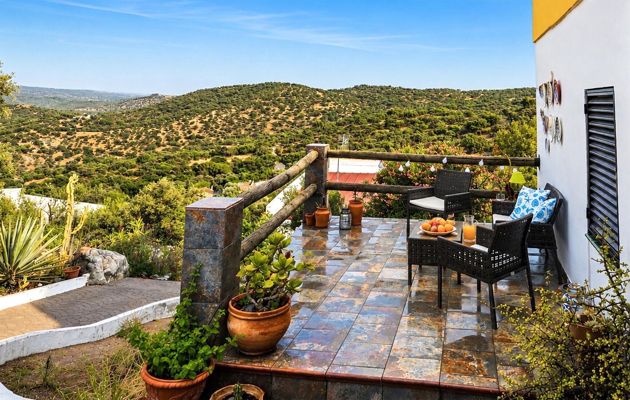Une terrasse aménagée avec du mobilier d’extérieur, des plantes en pot et une vue sur un paysage vallonné.