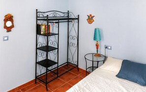 Une chambre avec une étagère en métal, un lit avec un oreiller bleu, une lampe et une horloge murale.
