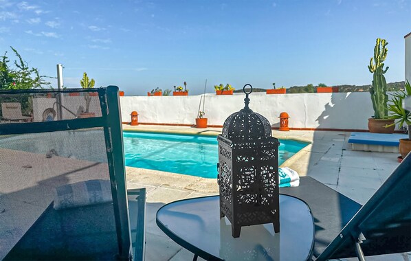 A poolside area with a glass table, a metal chair, and a decorative lantern.