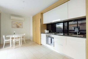 Eine moderne Küche mit weißen Schränken, ein Essbereich mit weißem Tisch und Stühlen und ein Fenster mit Blick nach draußen.