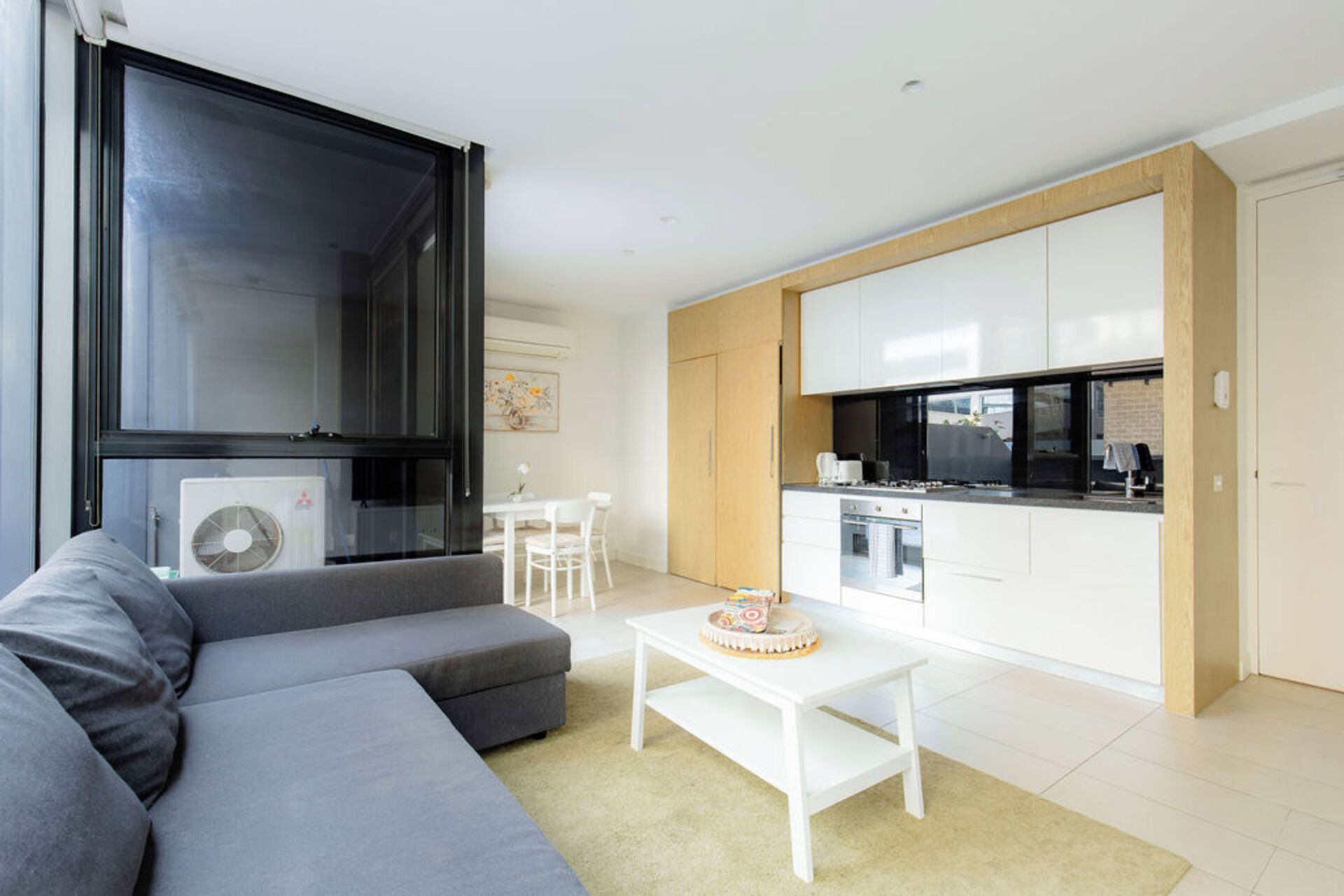 Un salon moderne avec un canapé gris, une table basse blanche et un coin repas comprenant une petite table et des chaises.