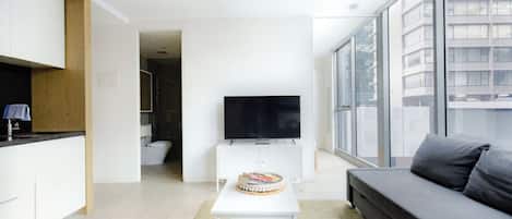 A modern living room with a flat-screen TV on a white stand, a grey sofa, and a small white table with a cake.