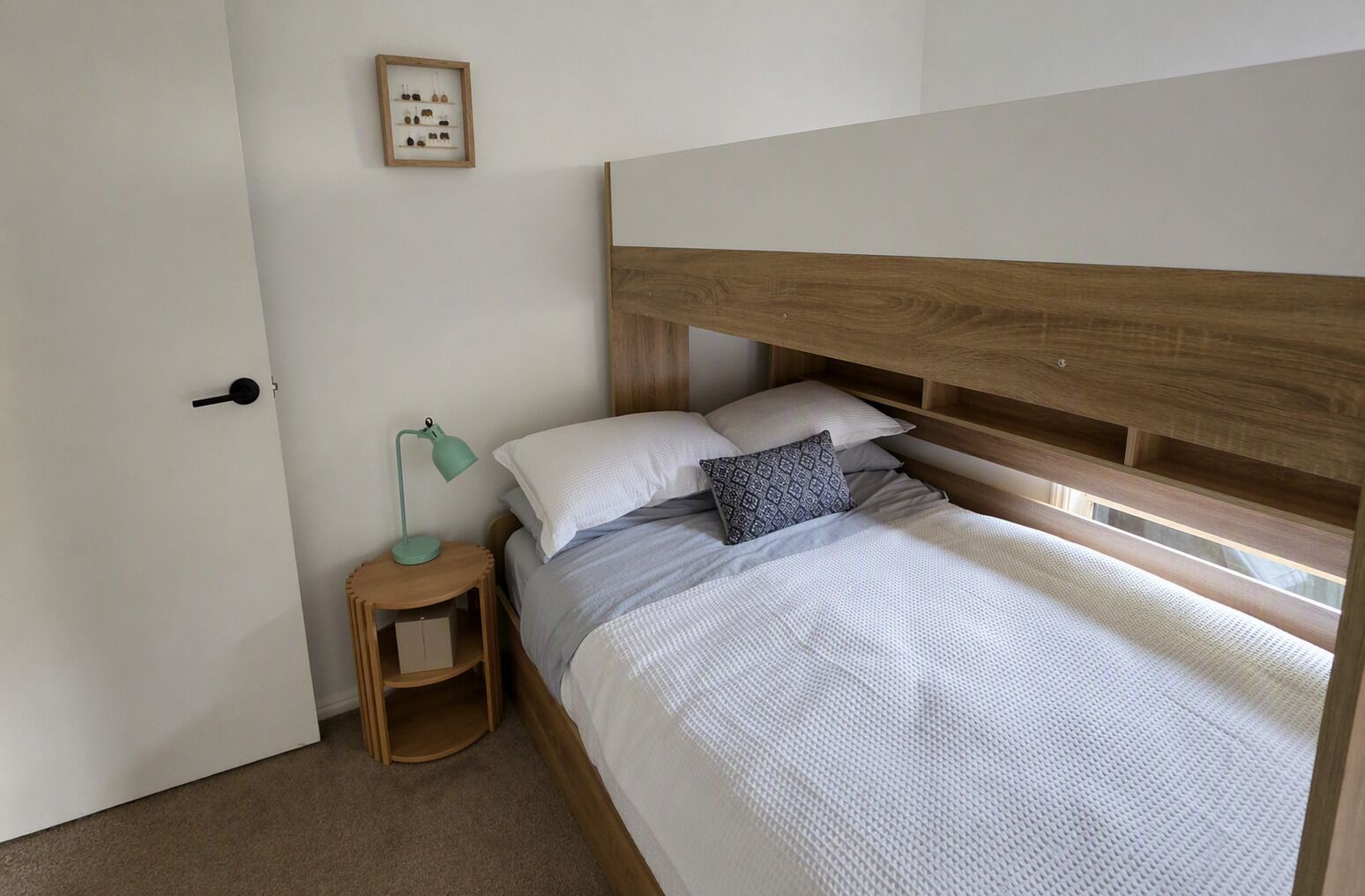 Un lit simple avec une tête de lit en bois, une table de chevet avec une lampe et un tableau encadré au mur.
