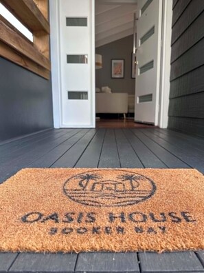 A doormat with 'OASIS HOUSE' text, a wooden door frame, and a dark floor. - Pool + Pet Friendly | 2 Min Walk to Beach & Cafés (Booker Bay)