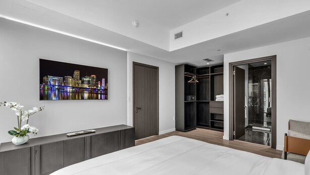A modern bedroom with a large bed, a cityscape painting, a wardrobe, and a walk-in closet. - Skyline Miami & Resort Amenities (Miami)