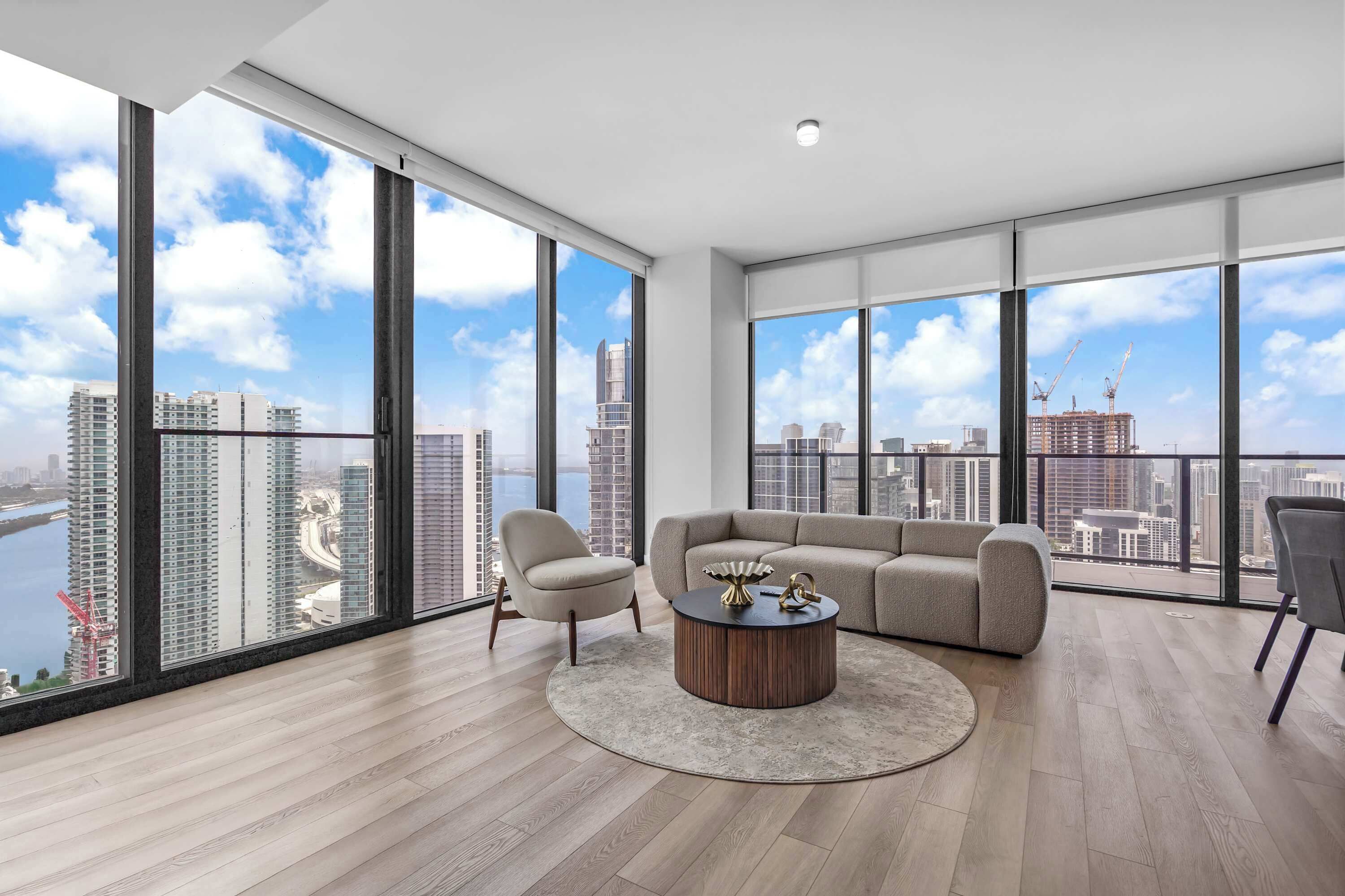 Un salón amplio con ventanas grandes, una mesa redonda, un sofá y un sillón.