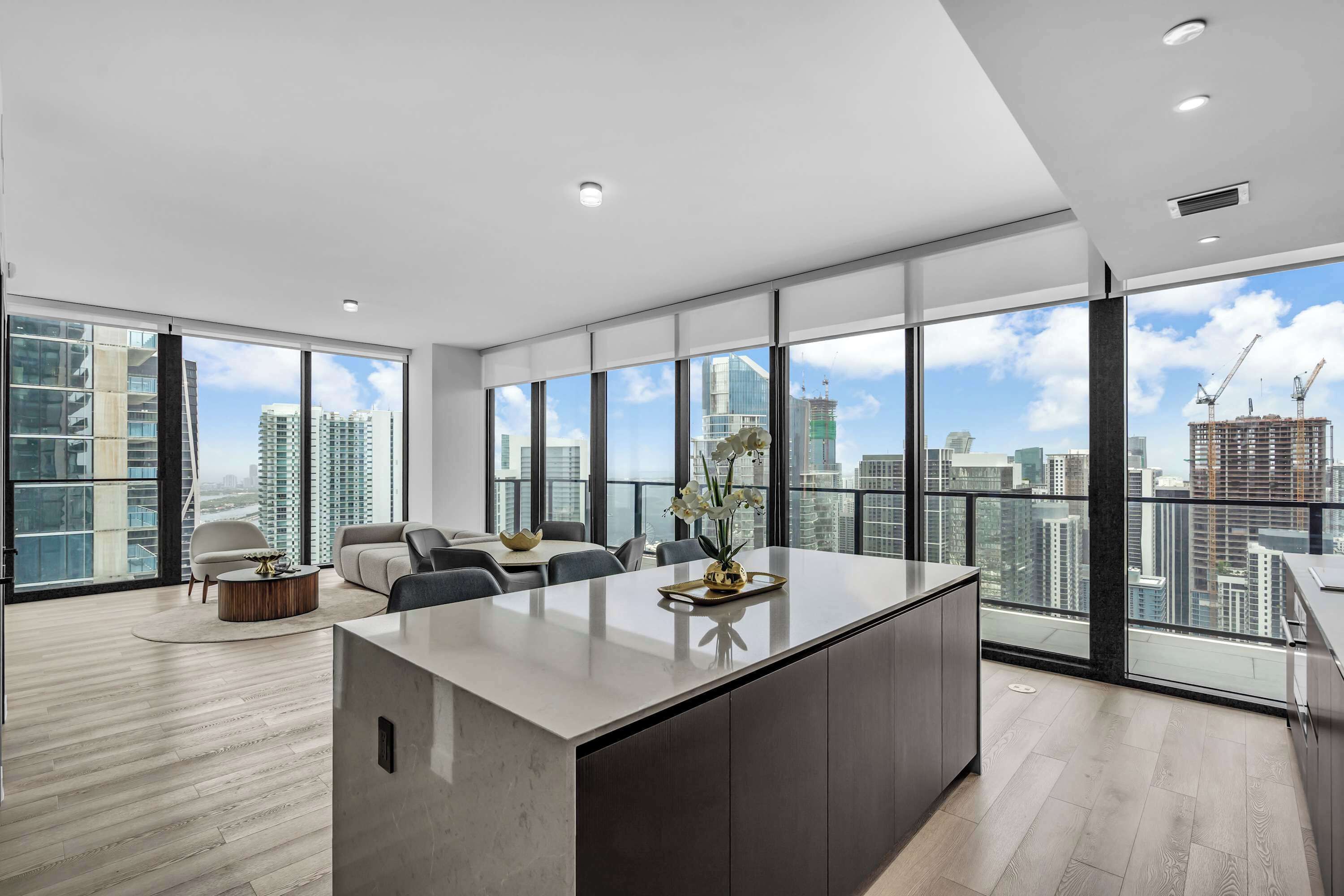 A modern interior with a central island, seating, and large windows offering a city view.
