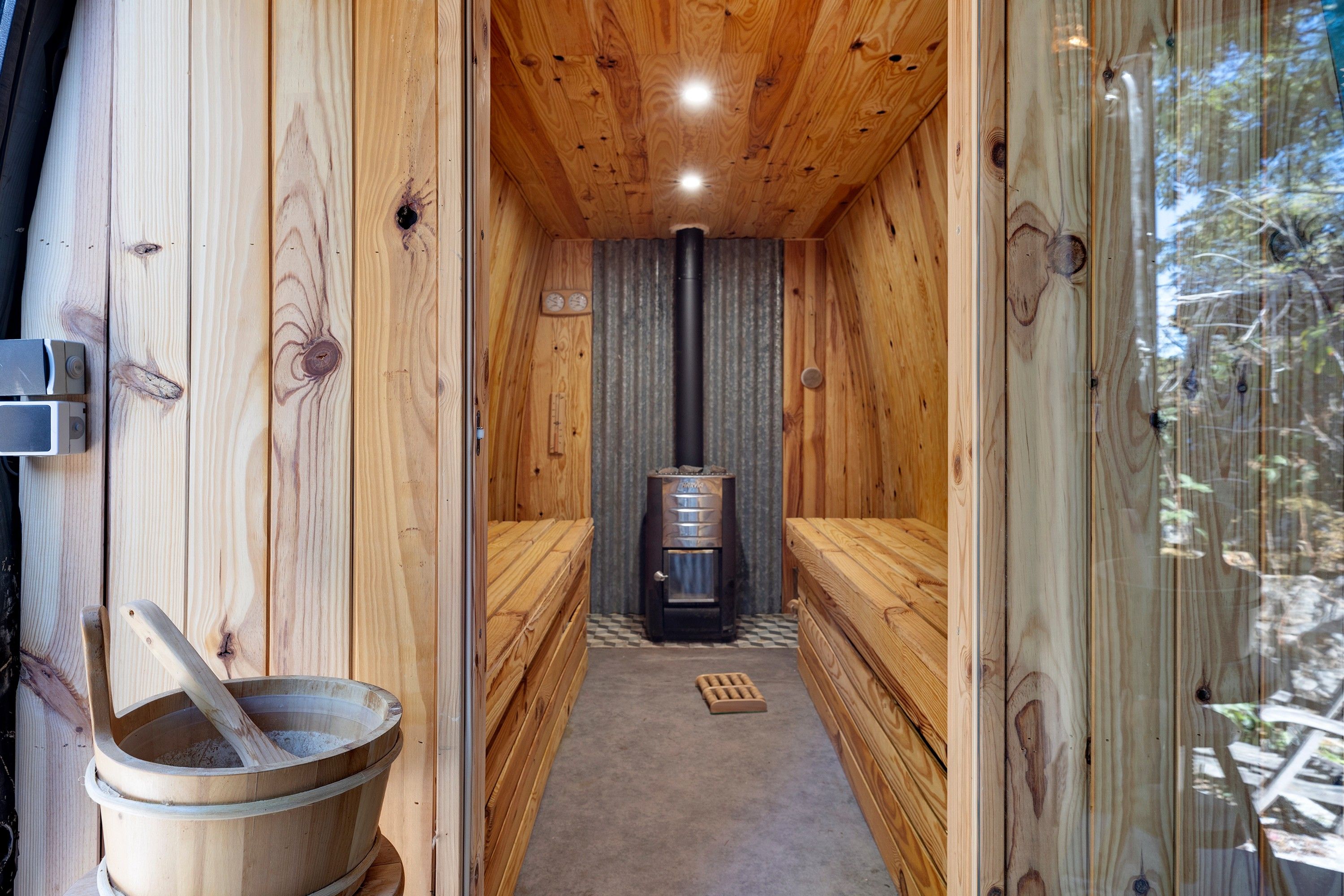 Uma sala de sauna com paredes de madeira, sauna, um balde de madeira e um tapete no chão.
