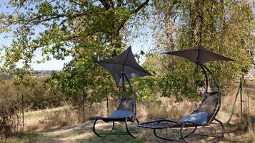 Twee buitsschommels met parasols, voor een achtergrond van bomen en een heldere lucht.