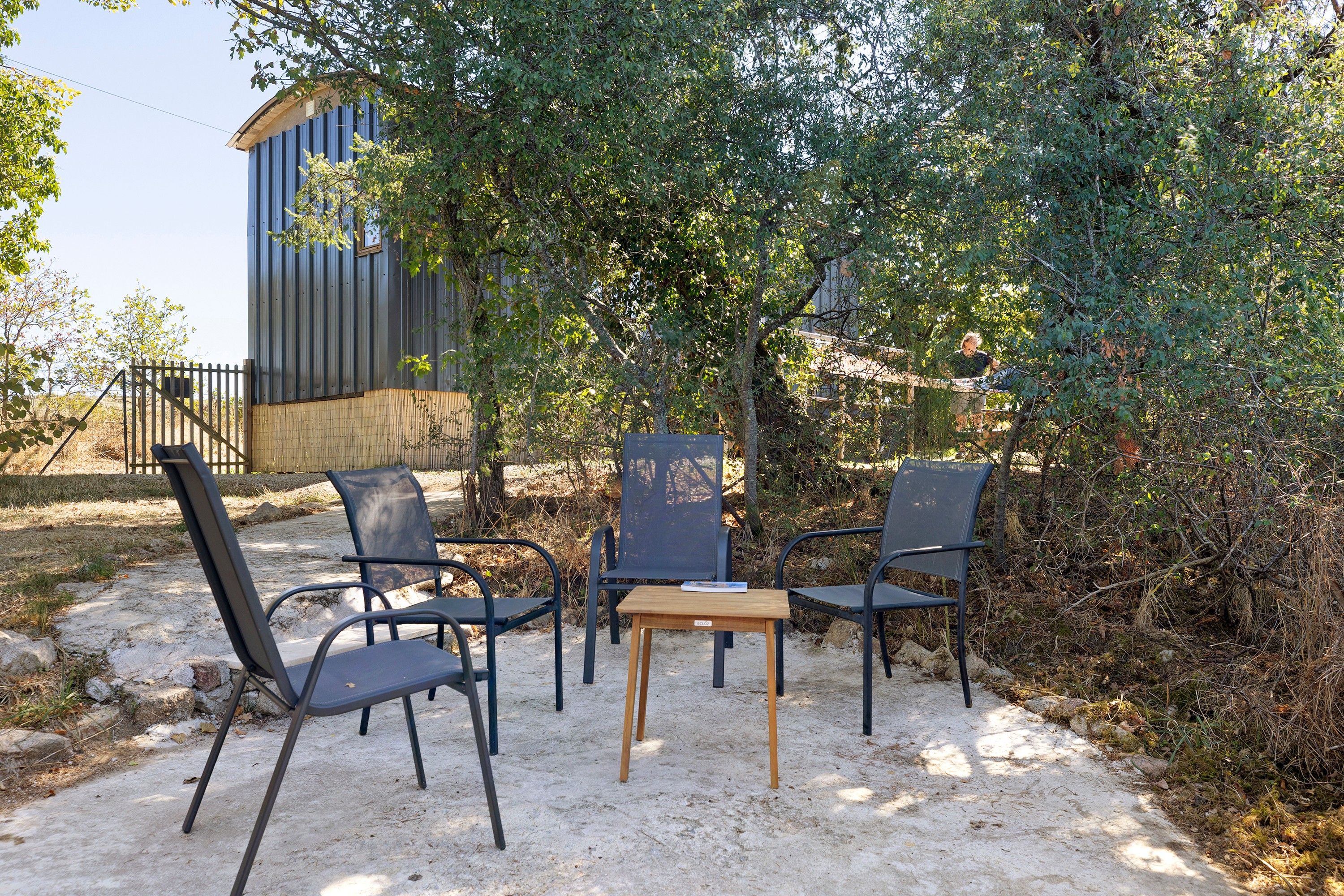 Un espace extérieur aménagé avec quatre chaises et une table, entouré d’arbres et d’un bâtiment.