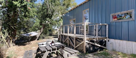 A rustic outdoor area with a wooden deck, picnic tables, and a corrugated metal building.