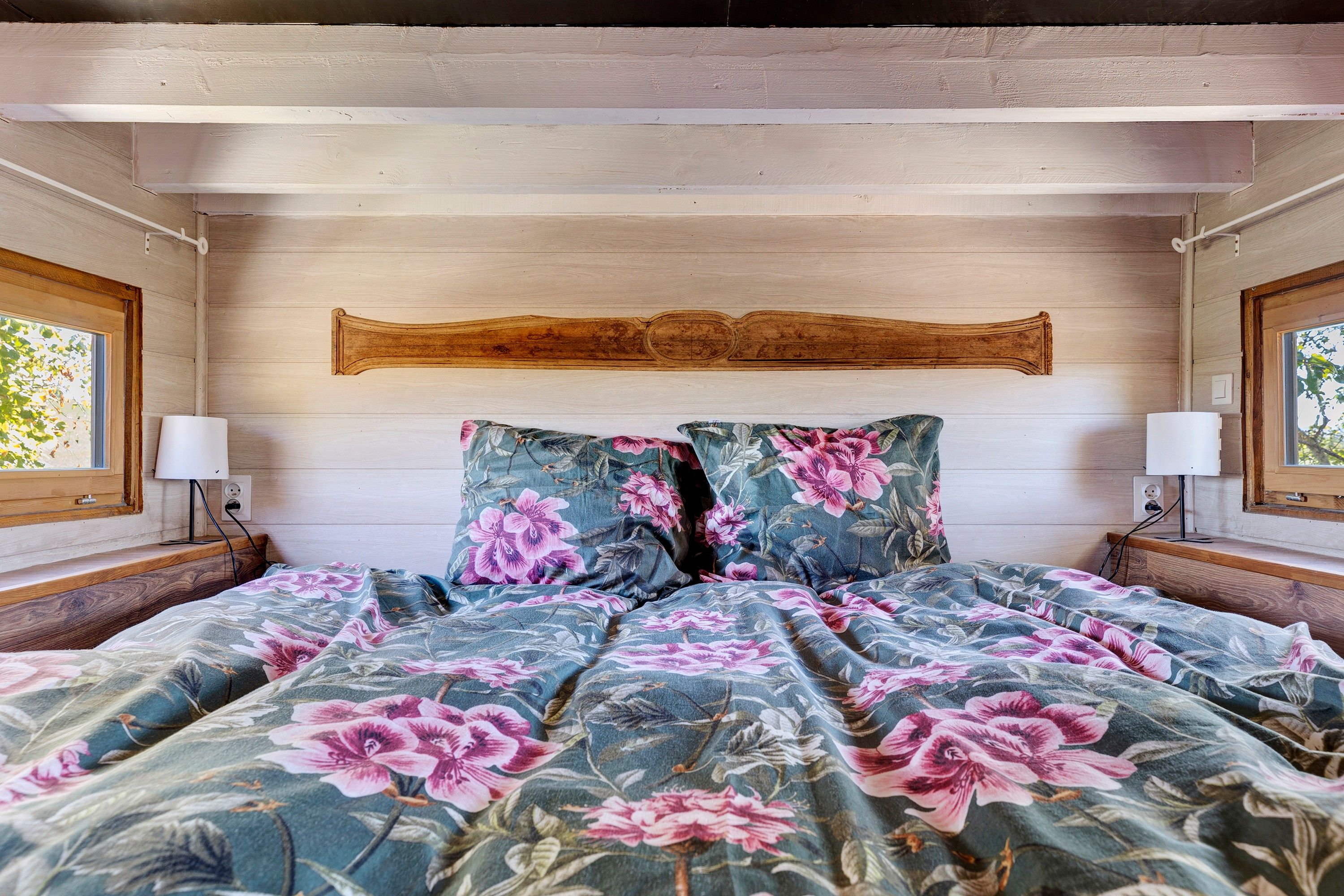 A bedroom with a wooden headboard, floral bedding, and two bedside lamps.