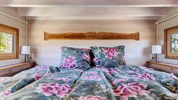 Quarto com cabeceira de madeira, roupa de cama florida e duas luminárias laterais.