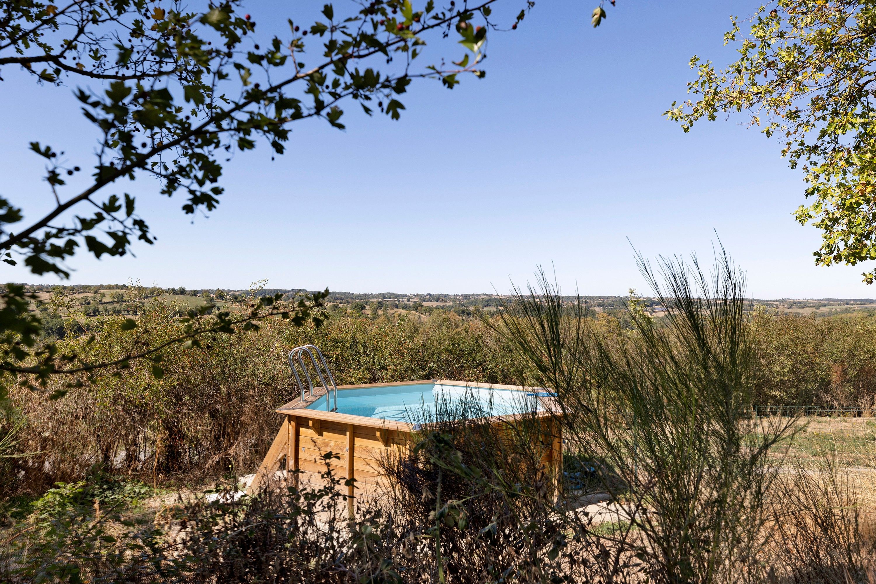 Estrutura de madeira com piscina, rodeada por vegetação e vista para uma paisagem distante.