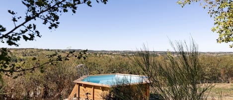 Eine Holzkonstruktion mit Schwimmbecken, umgeben von Vegetation und Blick auf eine entfernte Landschaft.