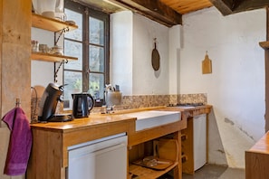 A rustic kitchen with wooden countertops, a coffee maker, a kettle, and a hanging wooden spoon.
