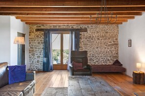 A room with a stone wall, wooden floor, a leather sofa, a wooden table, and a chair.