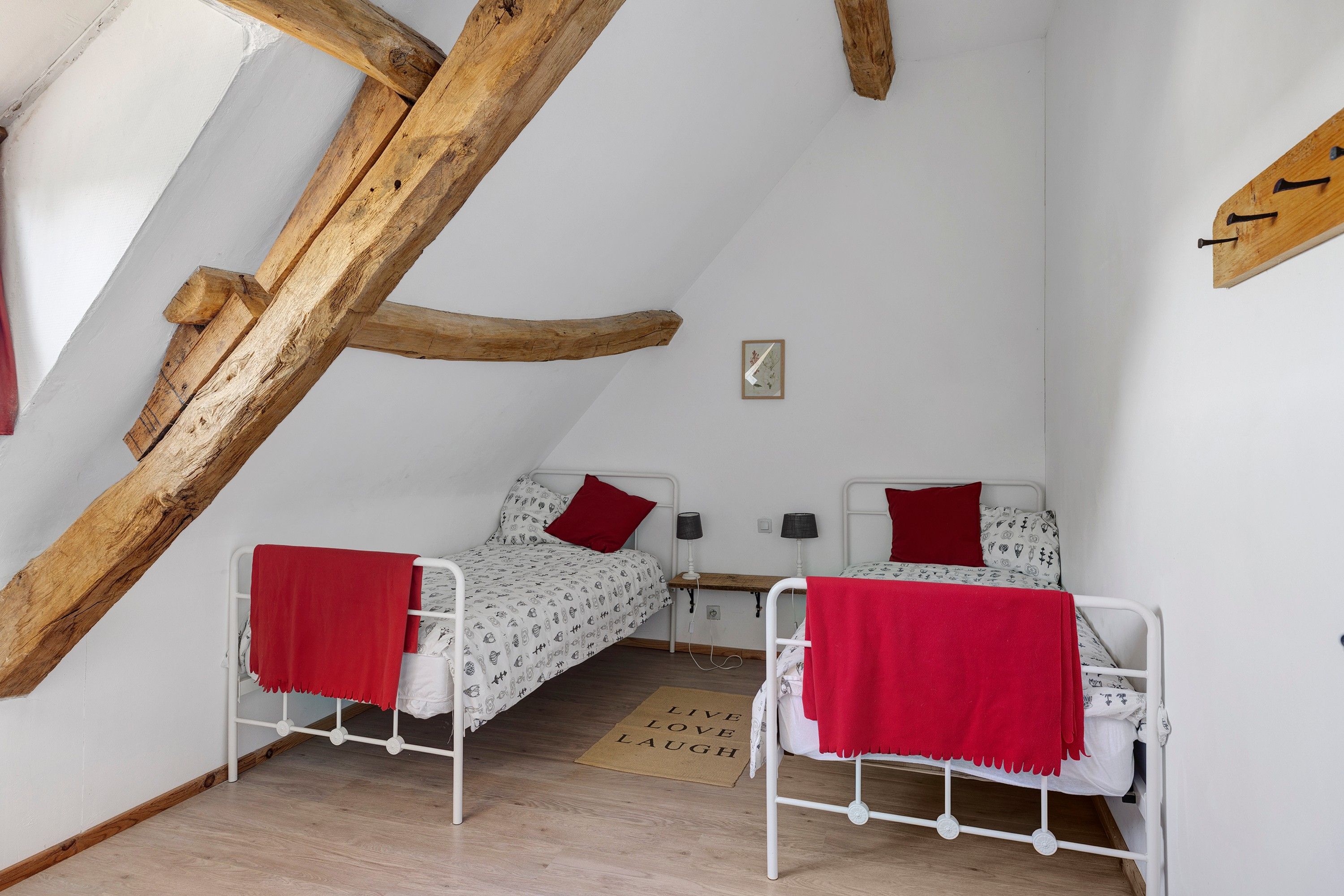 A small, cozy room with two single beds, a wooden ceiling beam, and a small wall-mounted picture.