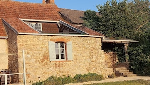 Ein Steinhaus mit geneigtem Dach, einem kleinen Fenster mit Rollläden und einer Treppe, die zu einem überdachten Bereich führt.