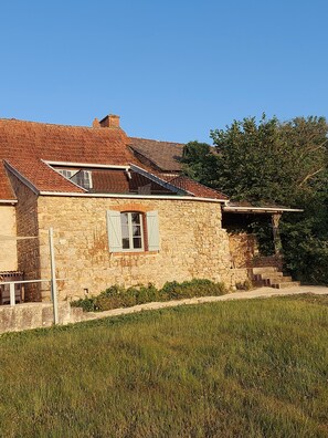 A stone building with a sloped roof, a small window with shutters, and a staircase leading to a covered area. - Cottage 'Gîte Grand-mère' with Private Pool, Terrace, and Wi-Fi (Charron)