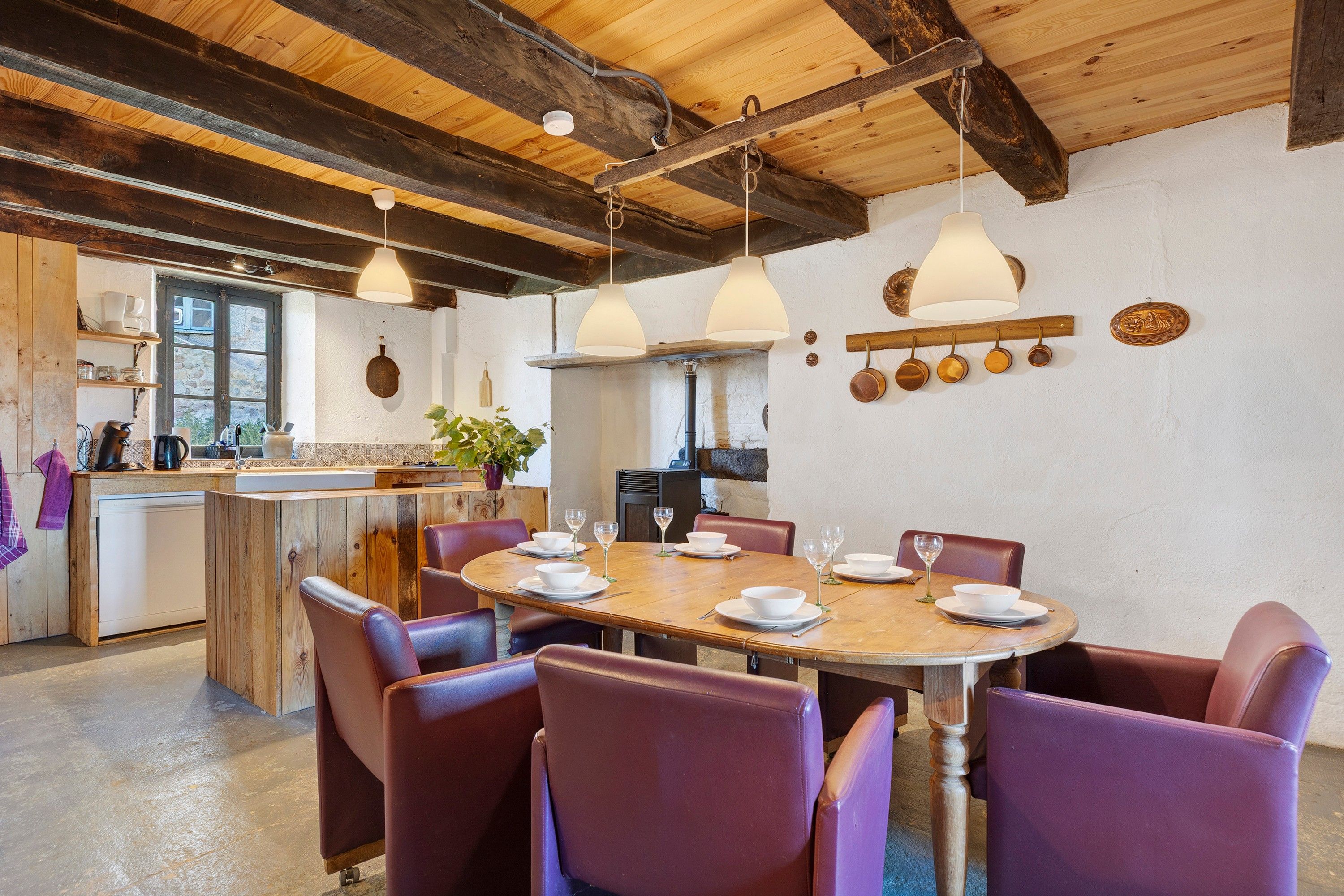 A rustic dining area with a wooden table, purple chairs, and hanging pendant lights.