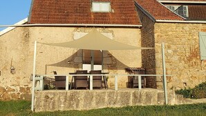 Ein Steinhaus mit Ziegeldach, eine überdachte Terrasse mit Tisch und Stühlen und ein kleines Fenster.
