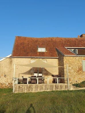 A stone building with a tiled roof, a covered patio with a table and chairs, and a small window. - Cottage 'Gîte Grand-mère' with Private Pool, Terrace, and Wi-Fi (Charron)