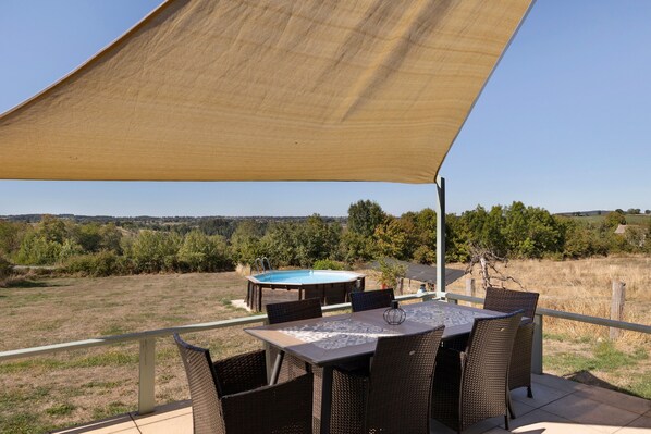 An outdoor patio with a table and chairs, a pool, and a view of the countryside.