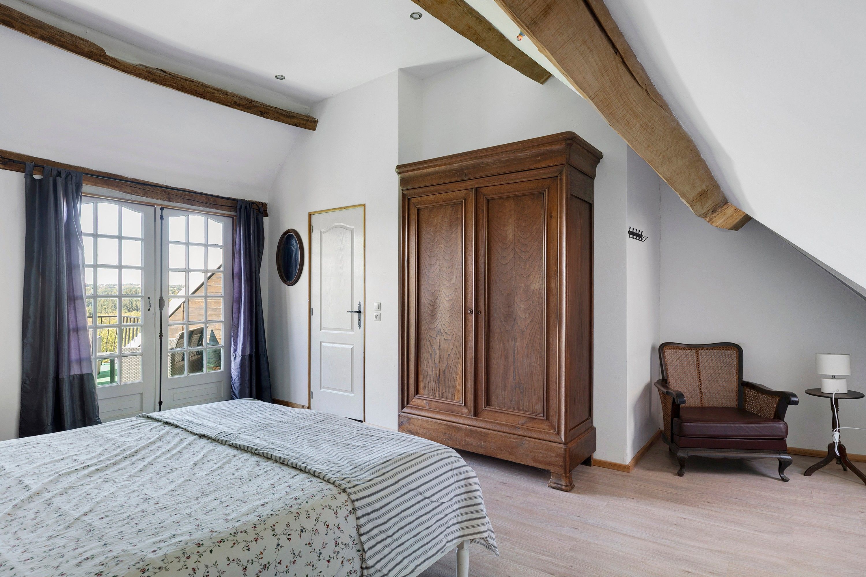 A bedroom with a bed, a wardrobe, a chair, and a desk with a lamp.