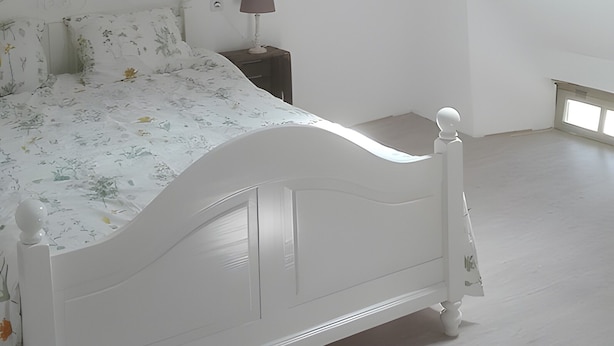 Ein Schlafzimmer mit einem weißen Bett, einem Nachttisch, einer Lampe und einem Oberlicht.