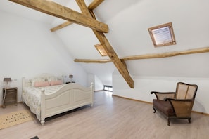 A bedroom with a sloped ceiling, a bed, a chair, and a small window.