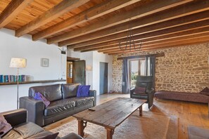 Ein rustikales Interieur mit freiliegenden Holzbalken, einer Steinwand, einem Ledersofa und einem Holztisch.
