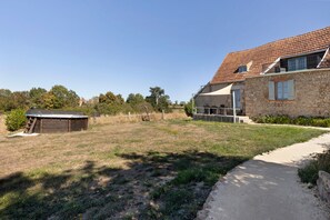 A stone house with a tiled roof, a fenced yard, and a clear sky.