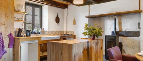 Una cocina rústica con vigas de madera, un lavavajillas blanco, una isla de madera y una silla roja.
