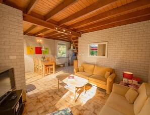 Ein gemütliches Wohnzimmer mit Holzbalkendecke, einer Couch, einem Couchtisch und einem Fernseher.