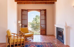 A room with a fireplace, a wicker chair, a floor lamp, and a view through an open door. - Stunning home in Santa Maria (Santa Maria)