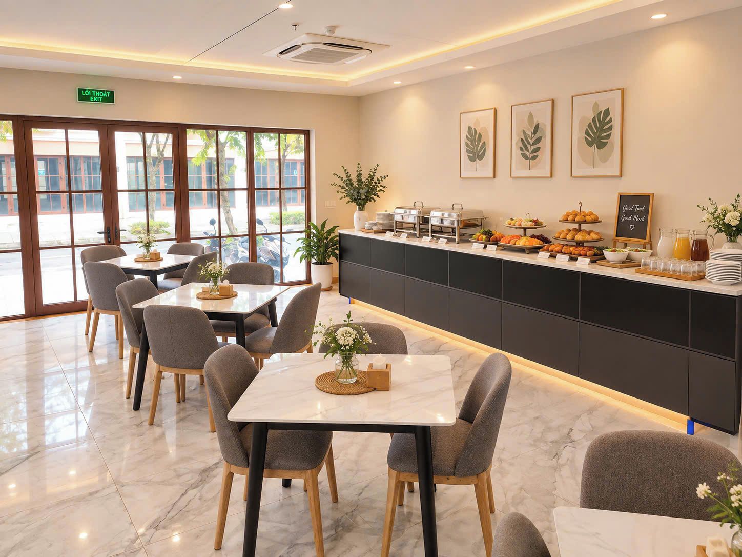 Comedor de hotel con mesas y sillas, un mostrador de buffet con comida y bebidas, y un cartel que indica la salida.