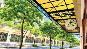 Uma passarela coberta com árvores e a fachada de um edifício ao fundo.