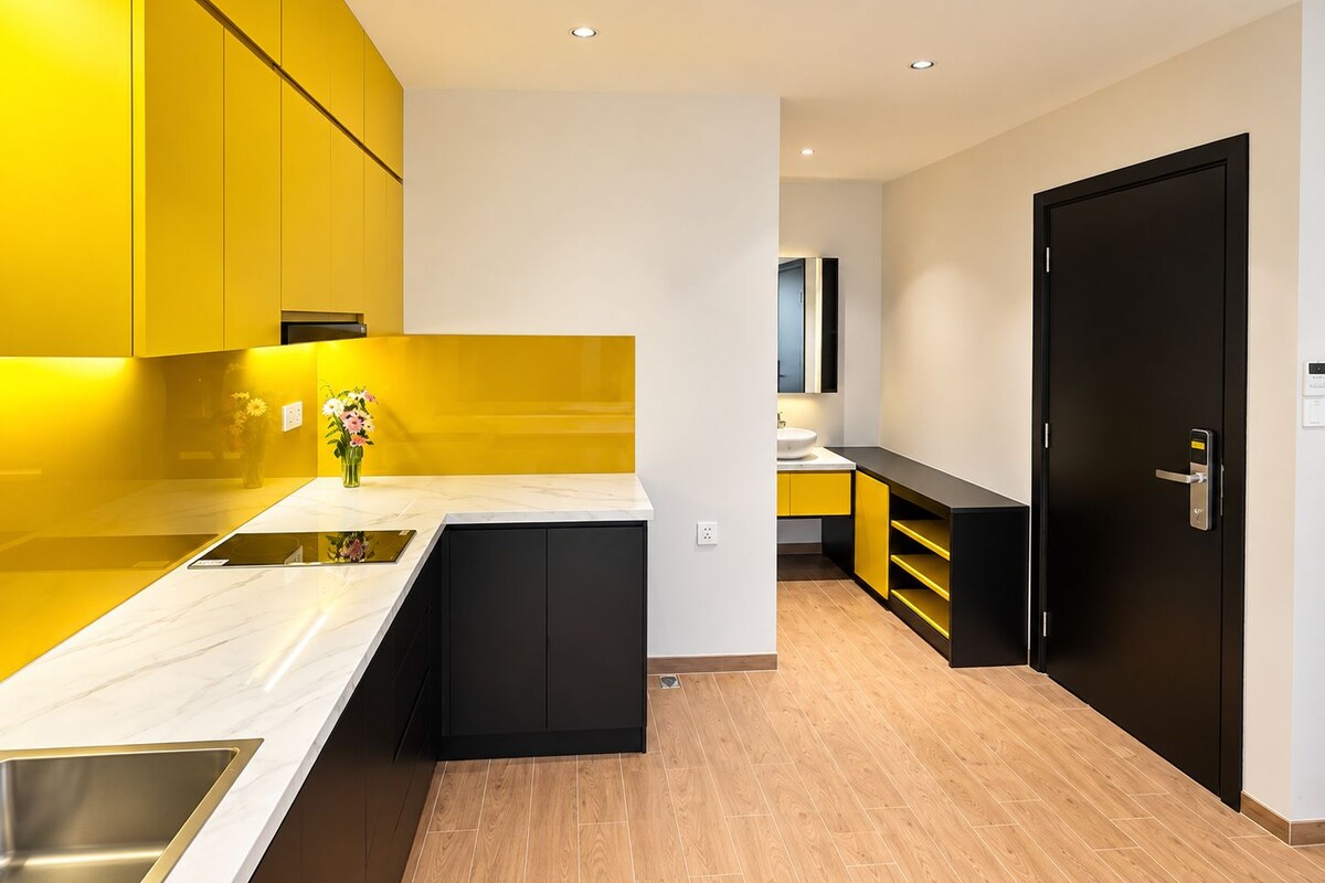 Een moderne keuken met gele kastjes, een wit aanrecht en een zwarte deur.