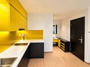 Een moderne keuken met gele kastjes, een wit aanrecht en een zwarte deur.