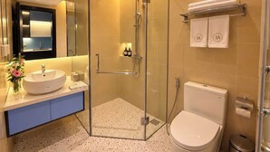 Un baño con un lavabo redondo, ducha con mampara de vidrio y un inodoro.