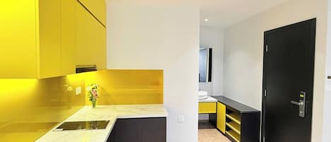 A modern kitchen with yellow cabinets, a marble countertop, and a black door.