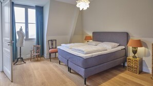 Ein Schlafzimmer mit einem Bett, zwei Stühlen, einer Schaufensterpuppe, einer Lampe und einem Schminktisch.