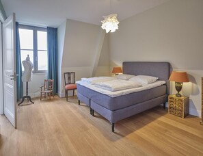 Ein Schlafzimmer mit einem Bett, zwei Stühlen, einer Schaufensterpuppe, einer Lampe und einem Schminktisch.