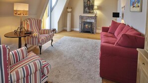 Ein gemütliches Wohnzimmer mit Kamin, gestreifte Sessel, einem roten Sofa und einem großen Fenster.