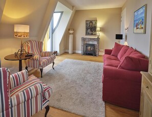Ein gemütliches Wohnzimmer mit Kamin, gestreifte Sessel, einem roten Sofa und einem großen Fenster.