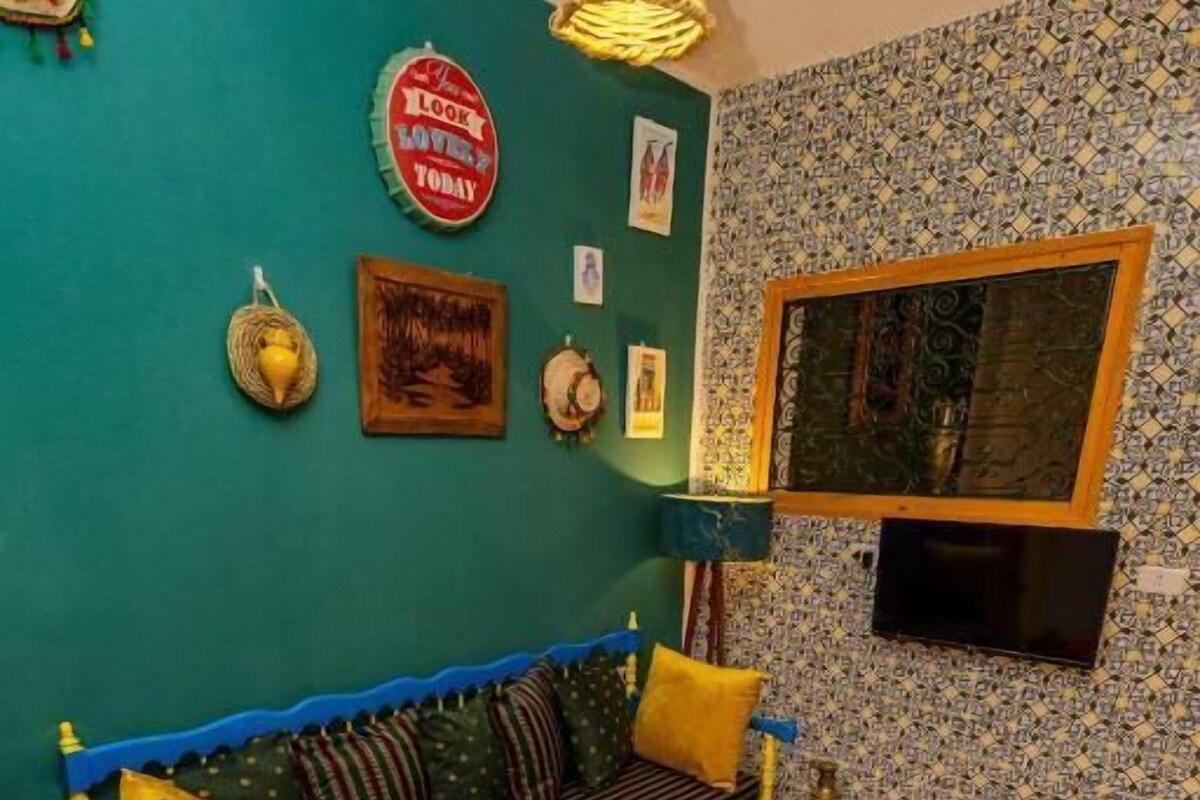 A room with a blue sofa, red ottomans, a patterned rug, and a wall with a clock and framed pictures.