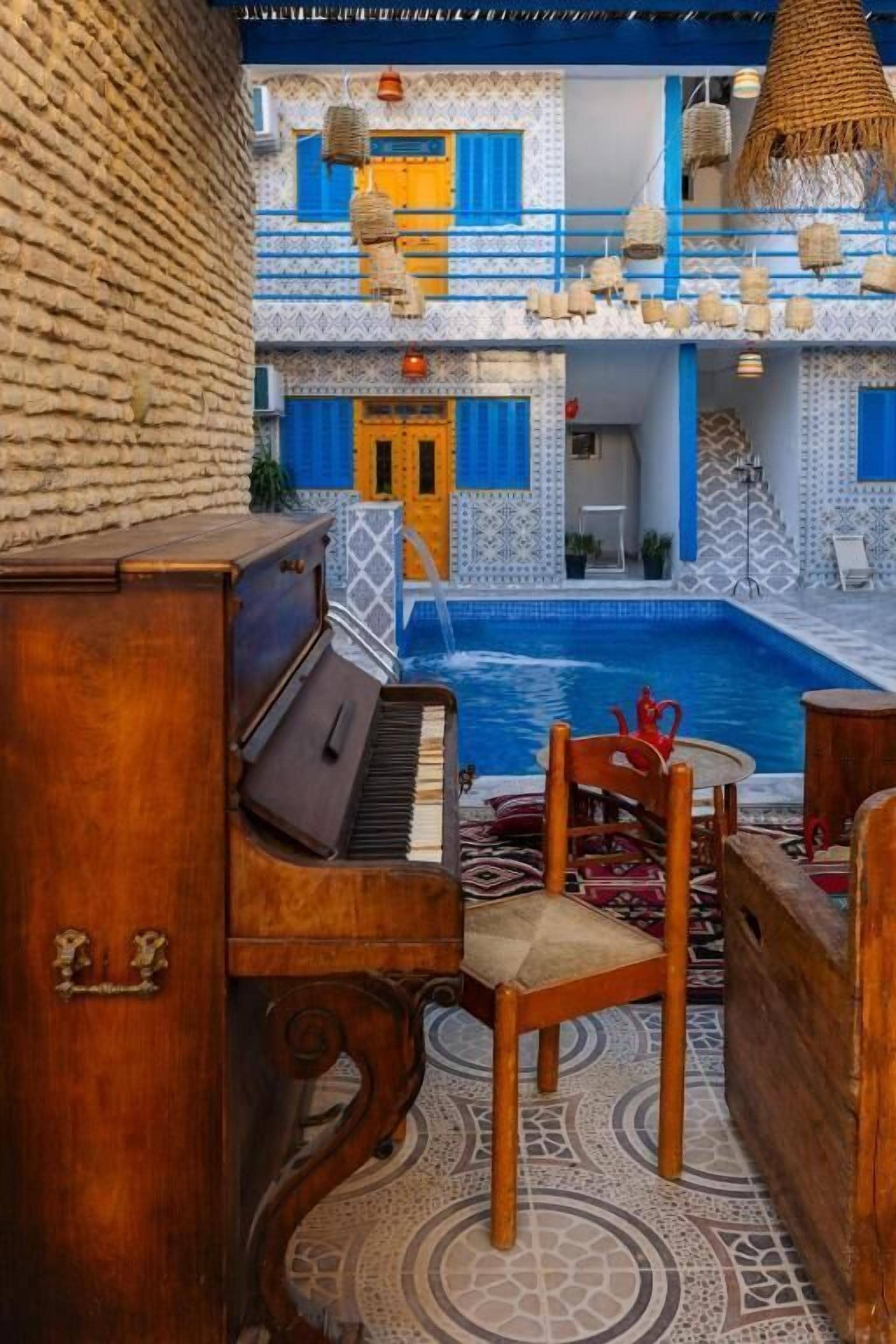 Zona junto a la piscina con un piano, una silla y vistas a un edificio con azulejos azules y blancos.