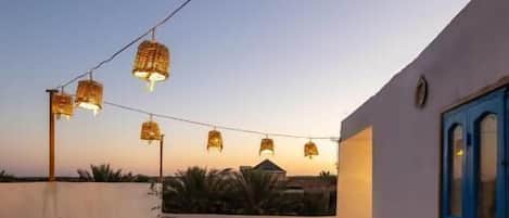 A rooftop terrace with a patterned rug, metal chairs, and hanging lights.